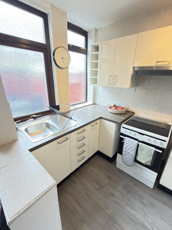 Small kitchen with cream cabinets, electric cooker, sink and window with frosted glass