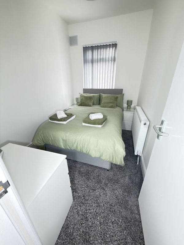 Compact bedroom with green bed, vertical blinds, gray carpet and white walls