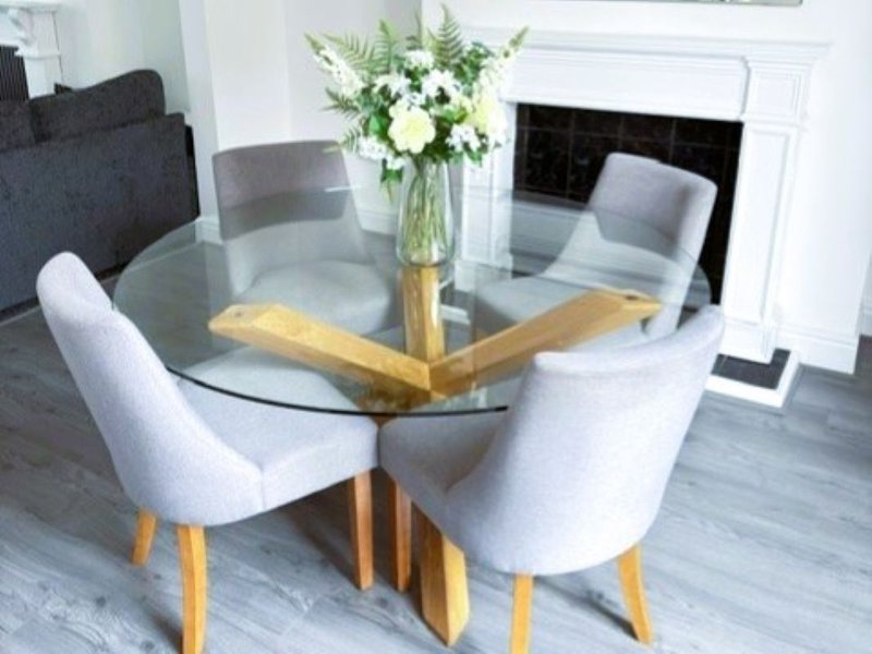 Modern dining room with round glass table, white upholstered chairs, and floral centerpiece