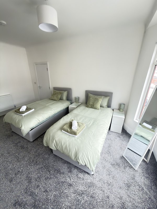 Bedroom with two single beds, green bedding, pendant light, and grey carpet flooring