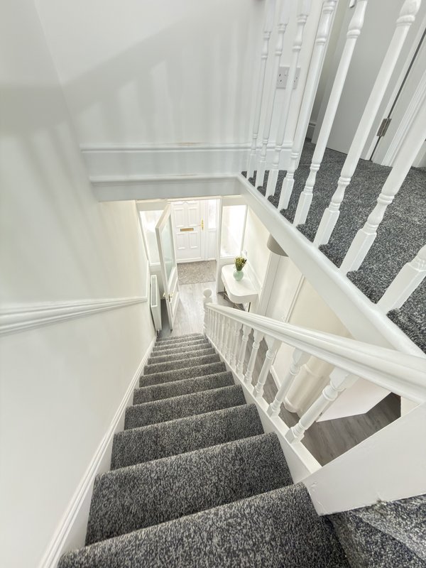 Staircase with grey carpet and white railings leading downward to entrance hallway