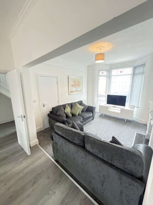 Modern living room with gray sofas, TV stand, wooden flooring, and bright windows