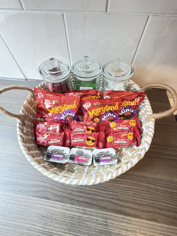 Wicker basket with snacks, candy packets, and glass jars on wooden counter