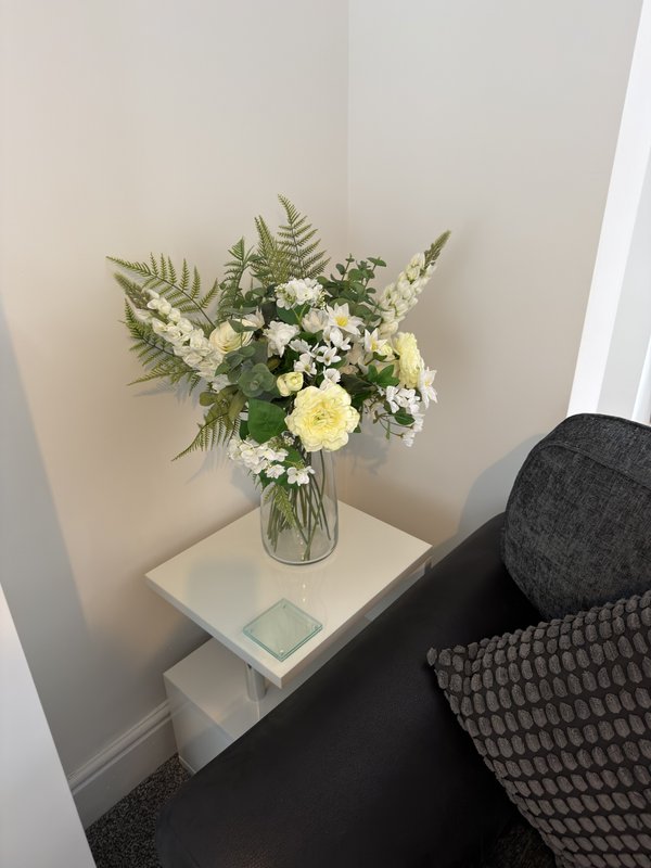 Bedside table with flower arrangement in glass vase and dark upholstered chair