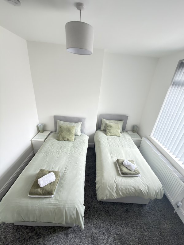 Twin bedroom with white beds, green cushions, pendant light and radiator