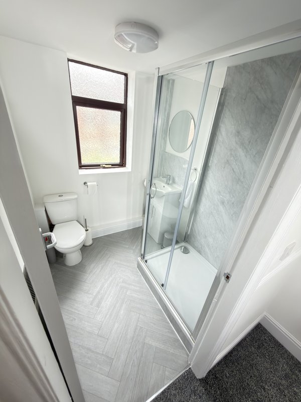 Modern bathroom with toilet, shower enclosure, window and herringbone tiled floor