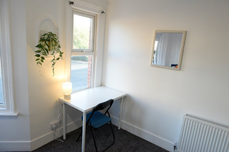 Small office nook with white desk, blue chair, hanging plant and mirror