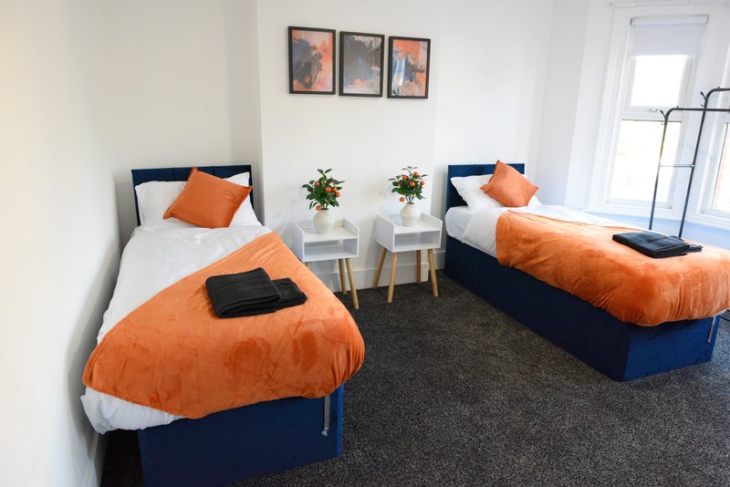 Twin bedroom with orange and navy bedding, white walls, framed artwork, and potted plants