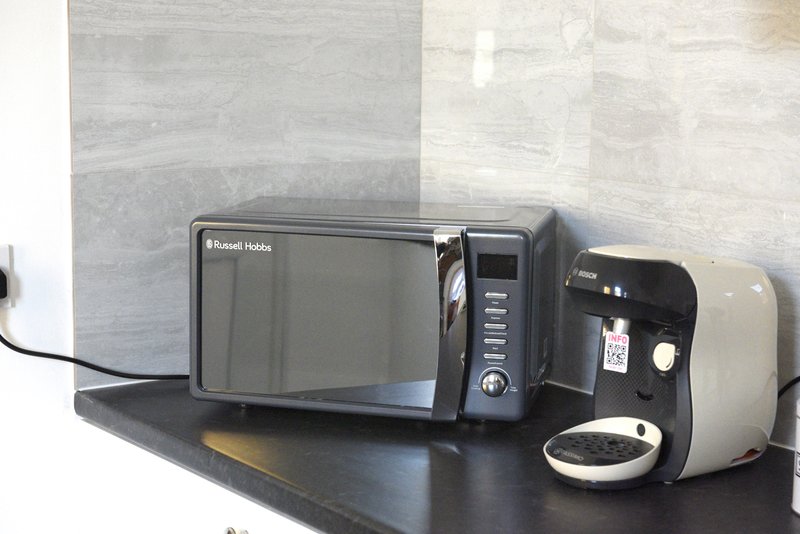 Kitchen counter with microwave, coffee maker, and toaster against tiled wall