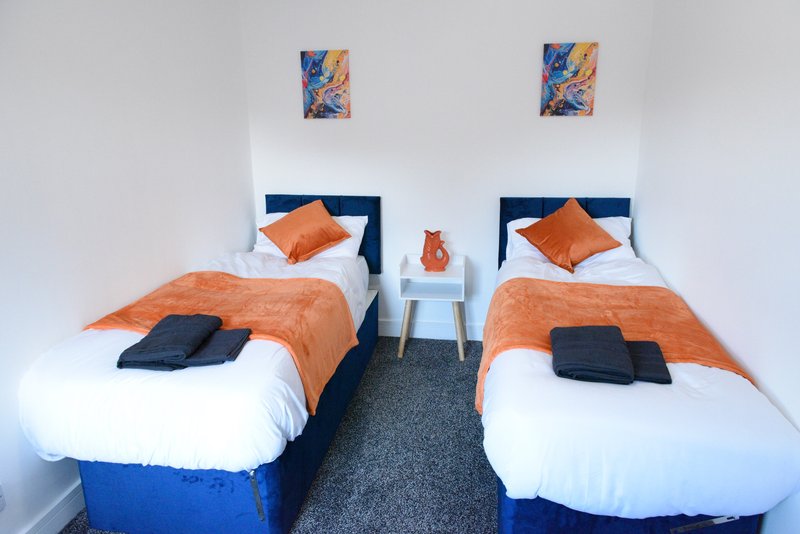 Twin bedroom with blue headboards, orange bedding, white pillows and abstract wall art