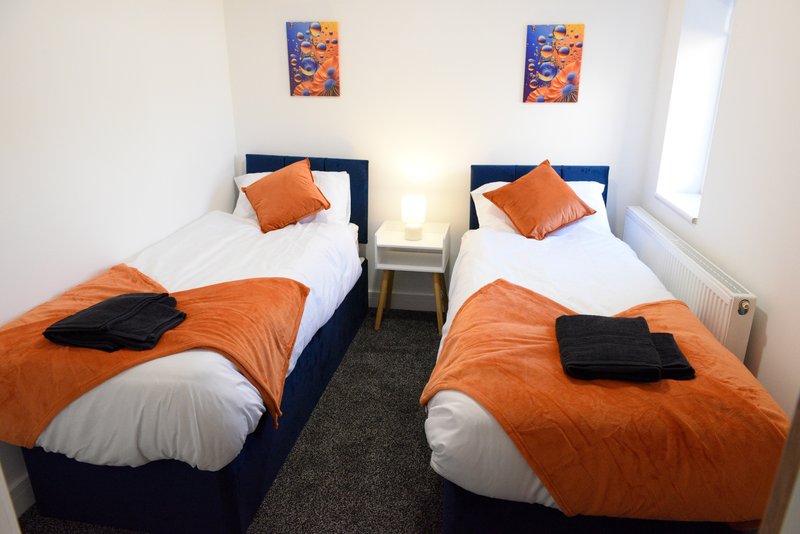 Twin bedroom with two single beds, orange bedding, navy headboards and wall art