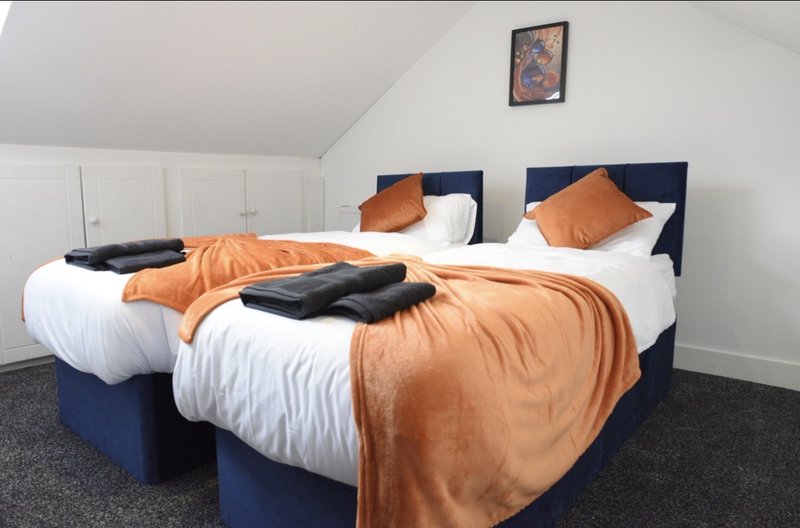 Bedroom with two single beds, orange throws, navy headboards and white bedding