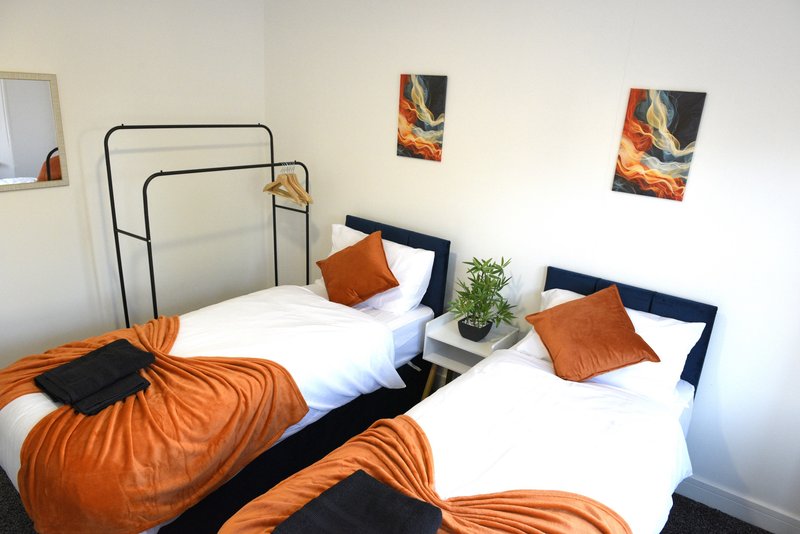 Bright bedroom with two single beds, orange and black bedding, wall art, and green plant