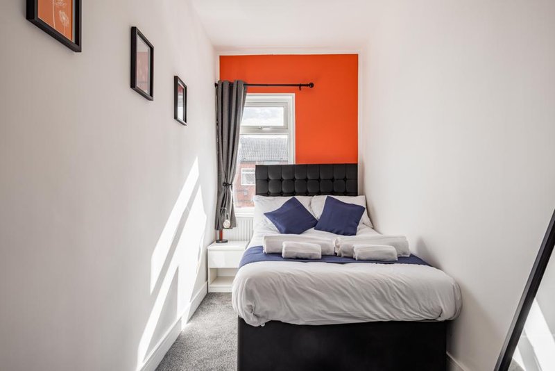 Second bedroom with small double bed, navy pillows, orange accent wall and window