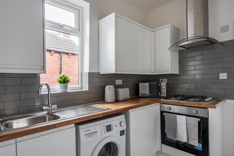 Modern kitchen with white cabinetry, grey tile splashback, wooden countertop, stainless steel sink and integrated appliances