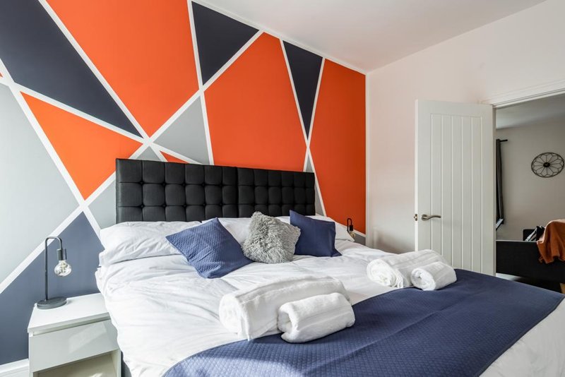 Modern bedroom with geometric orange and navy wall art, king size bed with white and blue bedding and cushions