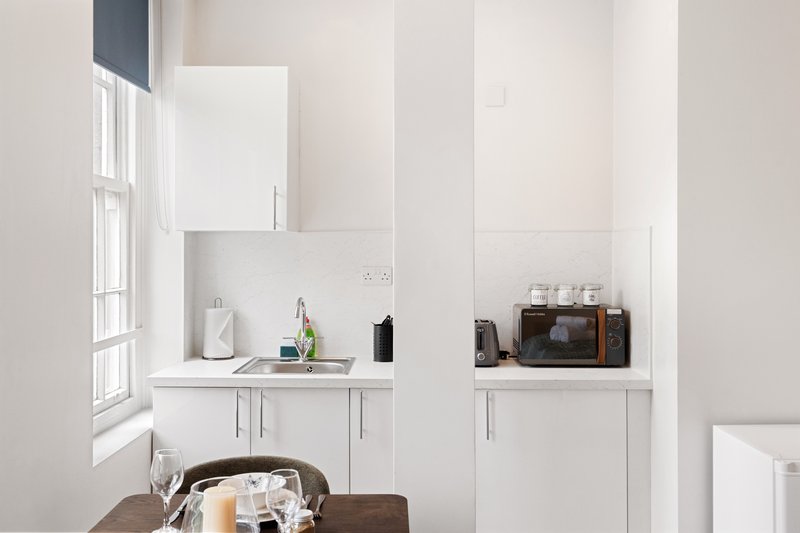 Compact white kitchen area with window, sink, appliances and open shelving