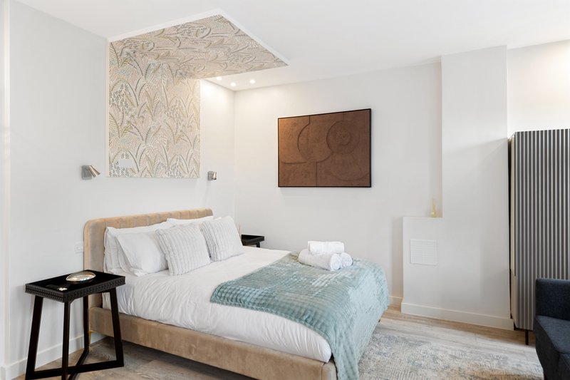 Modern bedroom with wooden bed frame, white bedding, geometric wall art, and minimalist furnishings