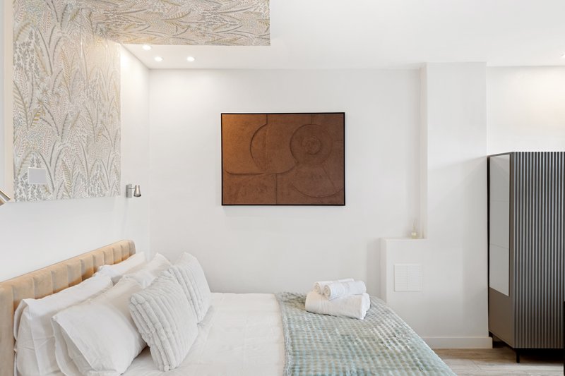 Bright bedroom with double bed, white bedding, abstract wall art, and modern wardrobe.