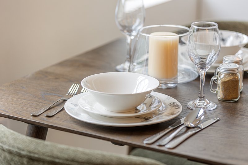 Dining table set with white plates, glasses, cutlery and condiments