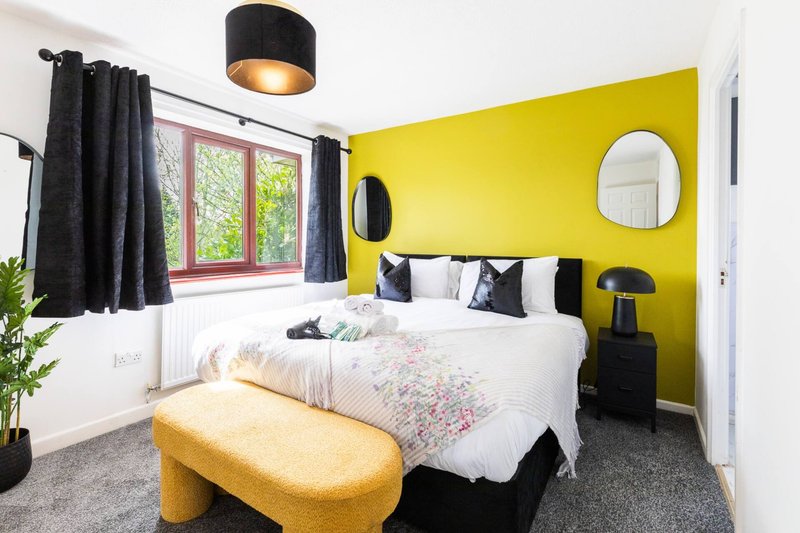 Bright bedroom with yellow accent wall, double bed, black pendant light and round mirror