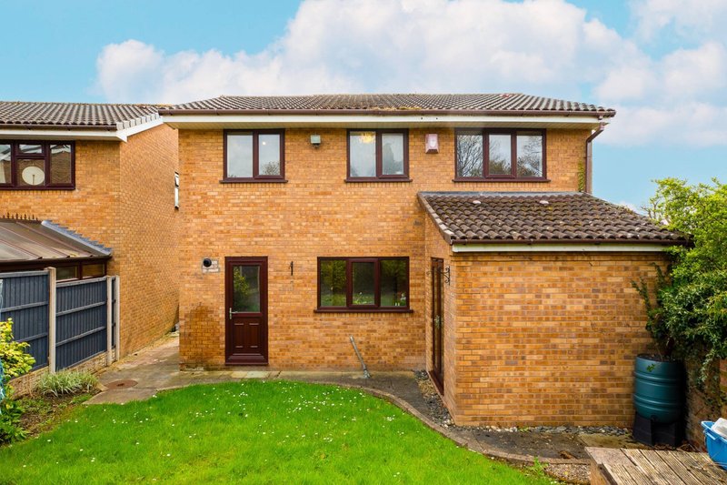 Brick suburban house with garden, patio area, and garage viewed from rear