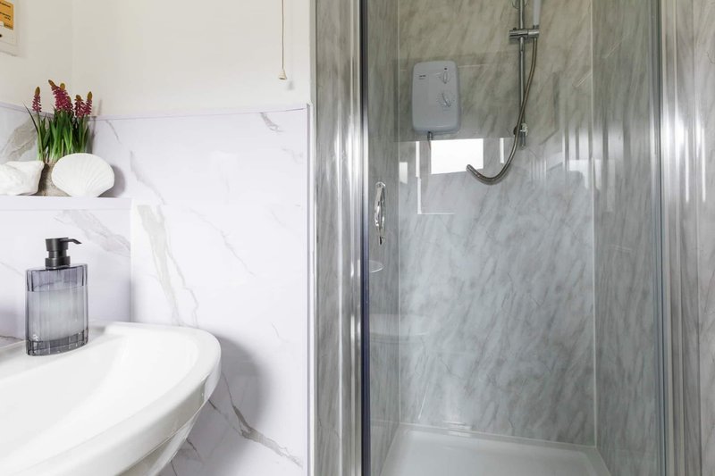 Modern bathroom with white sink, marble shower enclosure and decorative flowers