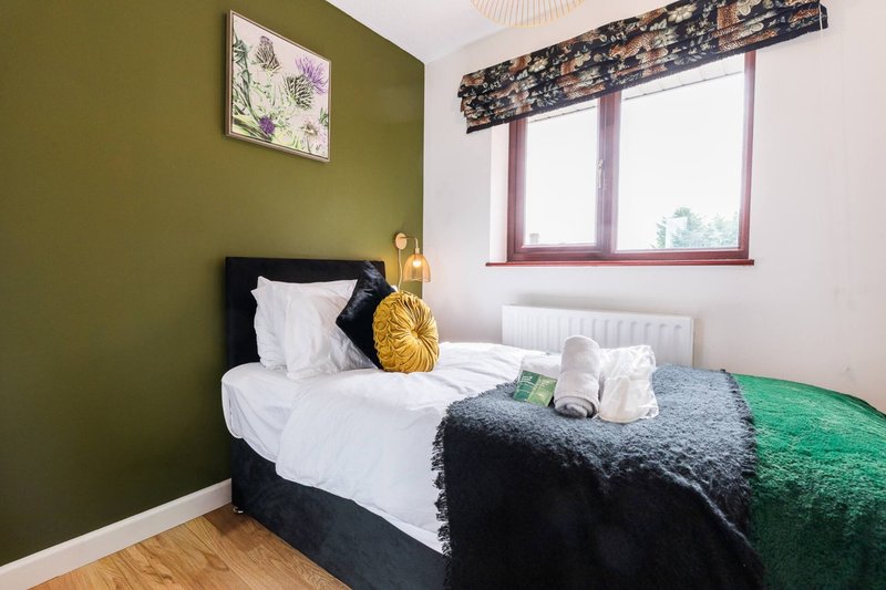 Bedroom with single bed, olive green wall, window with patterned blind and wooden floor