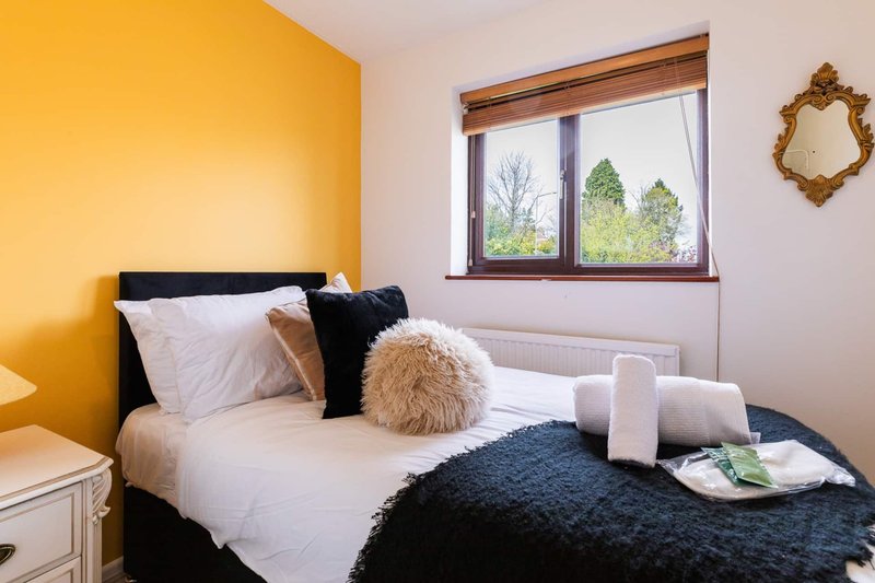 Bedroom with yellow accent wall, double bed, black headboard, cushions and fluffy throw
