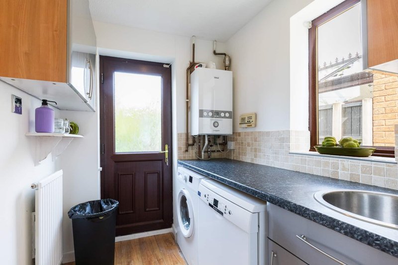 Galley kitchen with white appliances, dark countertop, sink, washing machine and door to garden