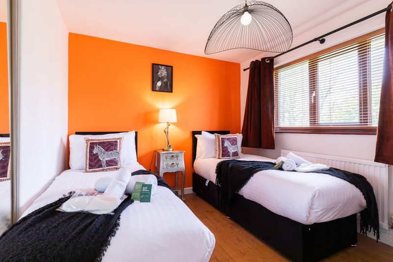 Twin bedroom with orange accent wall, two single beds, pendant light and wooden floor