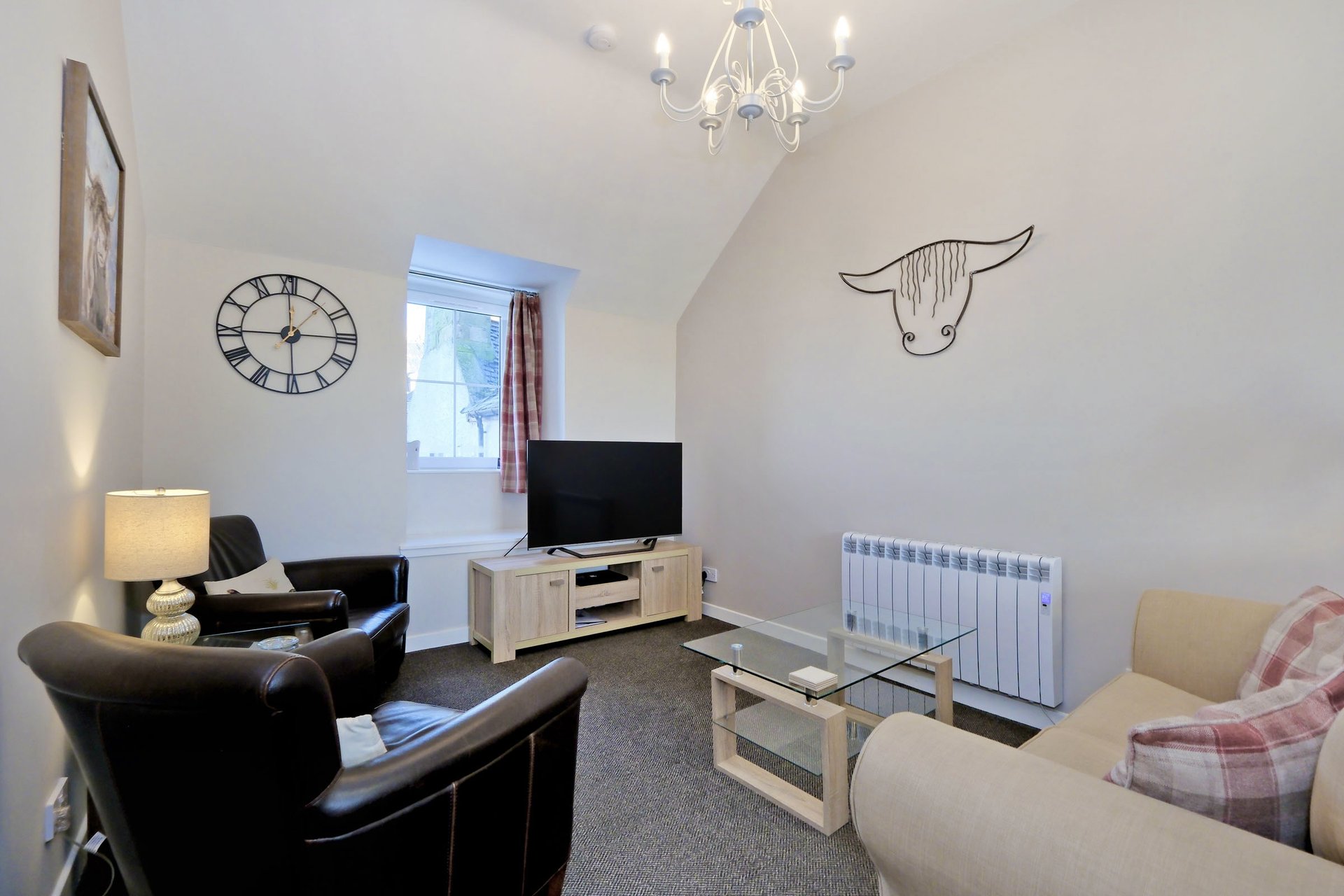 Living room with black armchair, TV on stand, cream sofa, wall clock and horned bull artwork