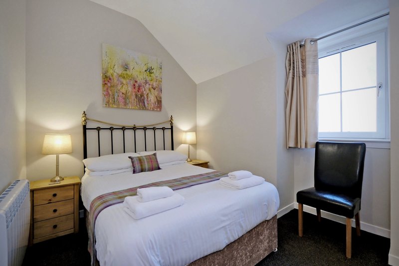 Bright bedroom with double bed, wooden nightstand, wall art, and television by window