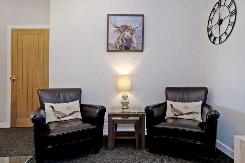 Living room with two black leather armchairs, small side table, wall-mounted clock and framed artwork