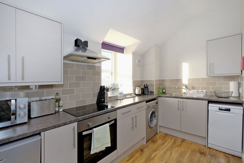 Modern kitchen with white cabinets, grey subway tile splashback, wooden flooring and integrated appliances