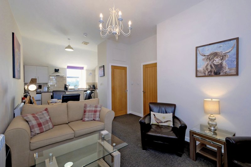 Open-plan living room with cream sofa, black armchair, glass coffee table and chandelier