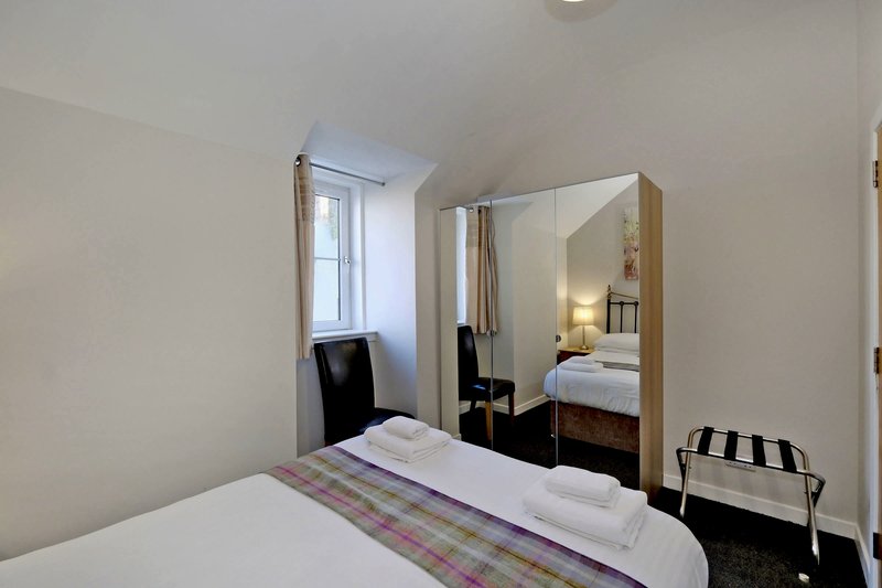 Bedroom with double bed, large mirror, black chair, and small window with natural light