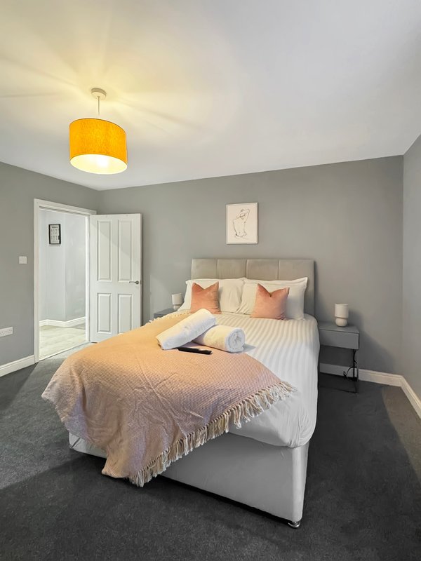 Bright bedroom with double bed, yellow pendant light, grey walls and white wardrobe