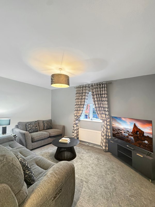 Spacious living room with grey sofas, patterned curtains, ceiling light and wall-mounted TV