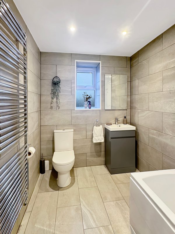 Modern bathroom with toilet, sink vanity, heated towel rail and tiled walls