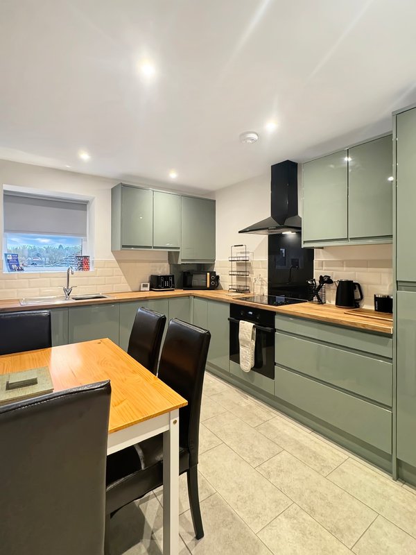Modern kitchen with sage green cabinetry, wooden worktops, dining table and black appliances
