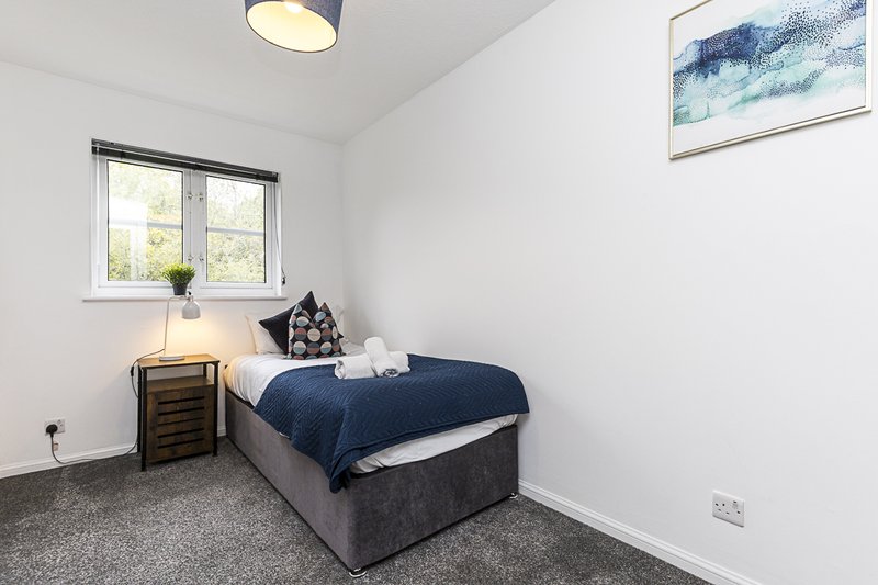 Bedroom with single bed, dark blue duvet, wooden nightstand and window with natural light