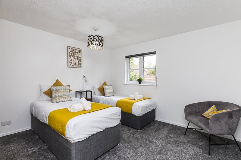 Twin bedroom with yellow and white bedding, grey carpet, armchair and window
