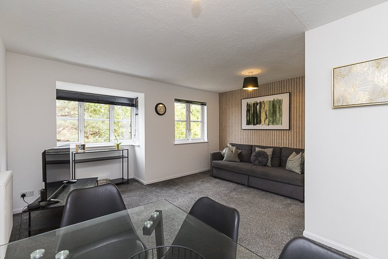 Open-plan living room with black furniture, dining table, desk, windows and wall art