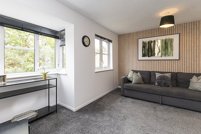 Modern living room with gray sofa, wooden accent wall, desk by window, and framed artwork