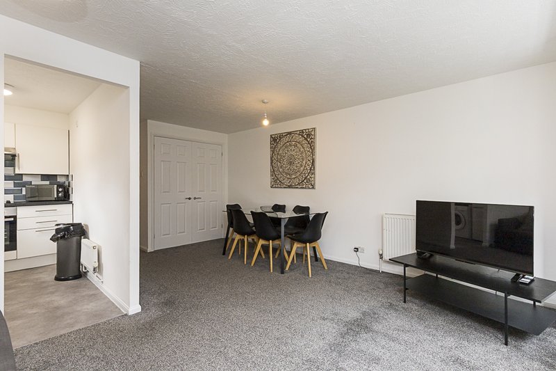 Open-plan living room with dining table, black chairs, TV, sofa and kitchen area visible