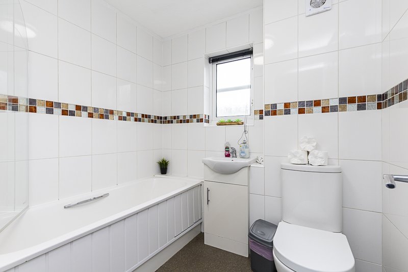 Clean bathroom with white tile walls, bathtub, sink, toilet and window