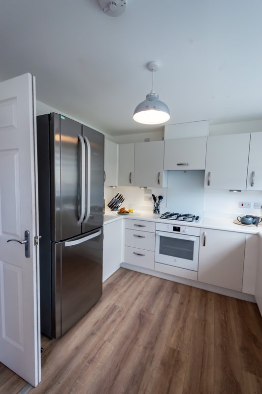 Modern kitchen with white cabinetry, stainless steel refrigerator, gas cooktop and pendant lighting