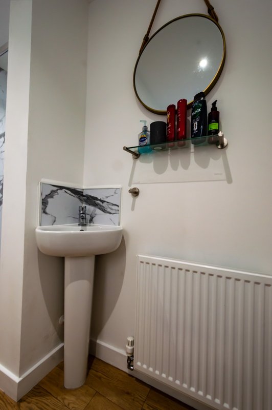 Bathroom corner with pedestal sink, round mirror, shelf with toiletries and radiator
