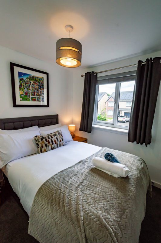 Modern bedroom with double bed, pendant ceiling light, framed artwork and window with black curtains